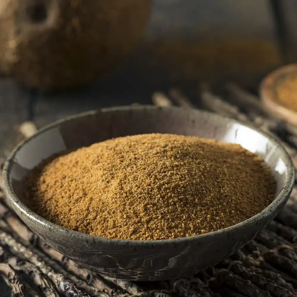 A bowl filled with coconut sugar on a rustic surface.