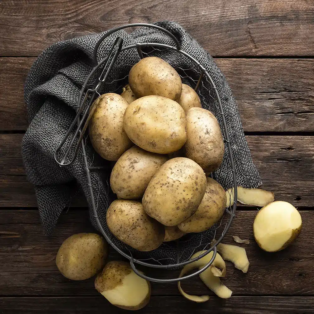 Basket of fresh potatoes on a rustic wooden surface.